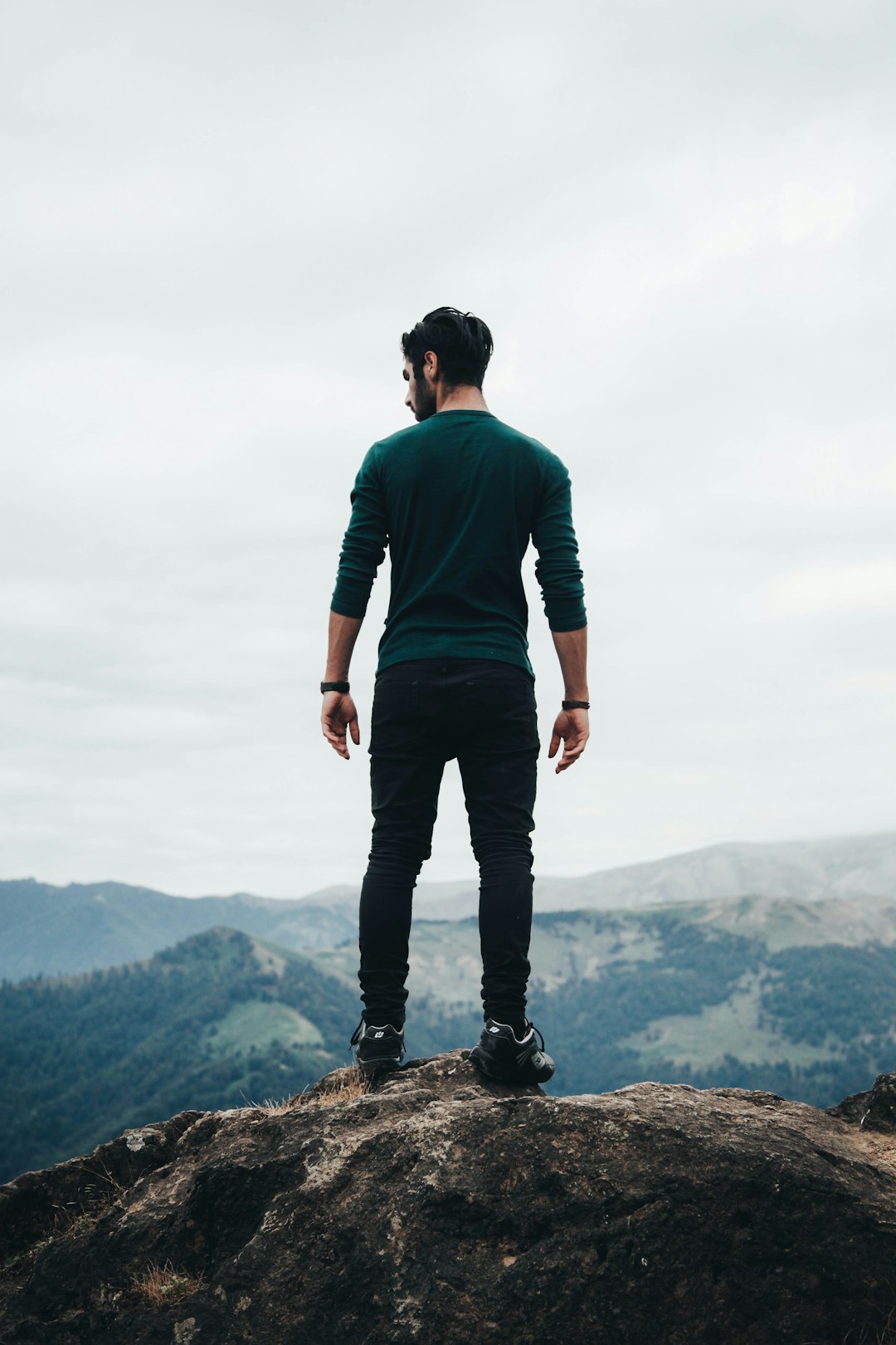 A Person Standing On Top Of A Rock Next To The Ocean With Clouds In The