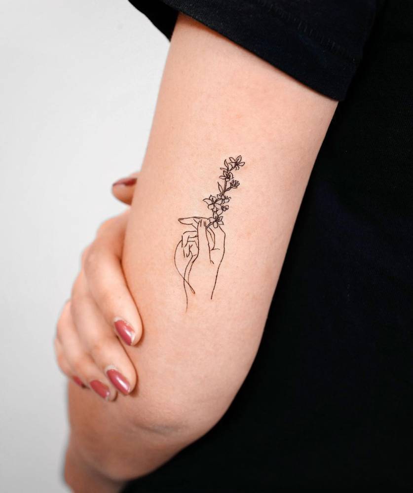 Fine Line Hand Holding Flowers Tattoo On The Upper Arm